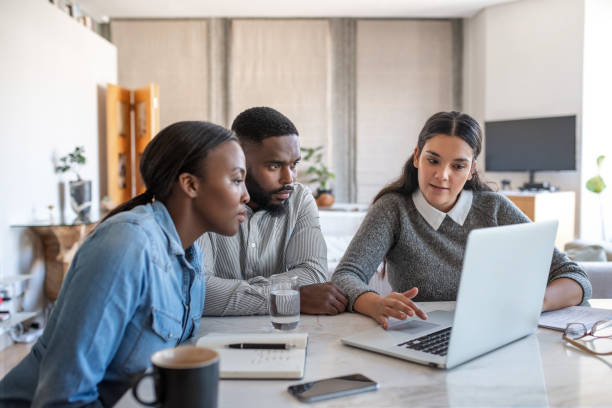 Financial planner going over savings plans on a laptop with a young African American couple at a table in their living room at home